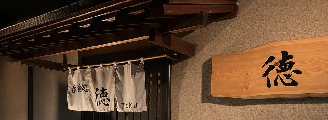 夜の店構え。「呑喰処 徳 Toku」ののれんと、「徳」と書かれた木の看板